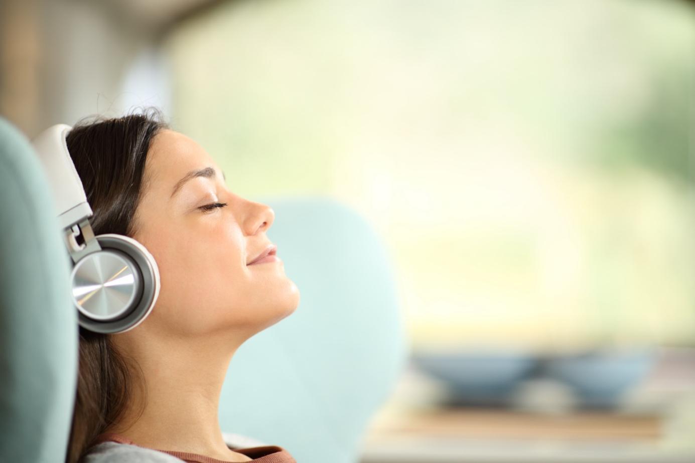 Eine Frau entspannt sich mit geschlossenen Augen in einem hellblauen Stuhl, während sie Musik über Kopfhörer hört