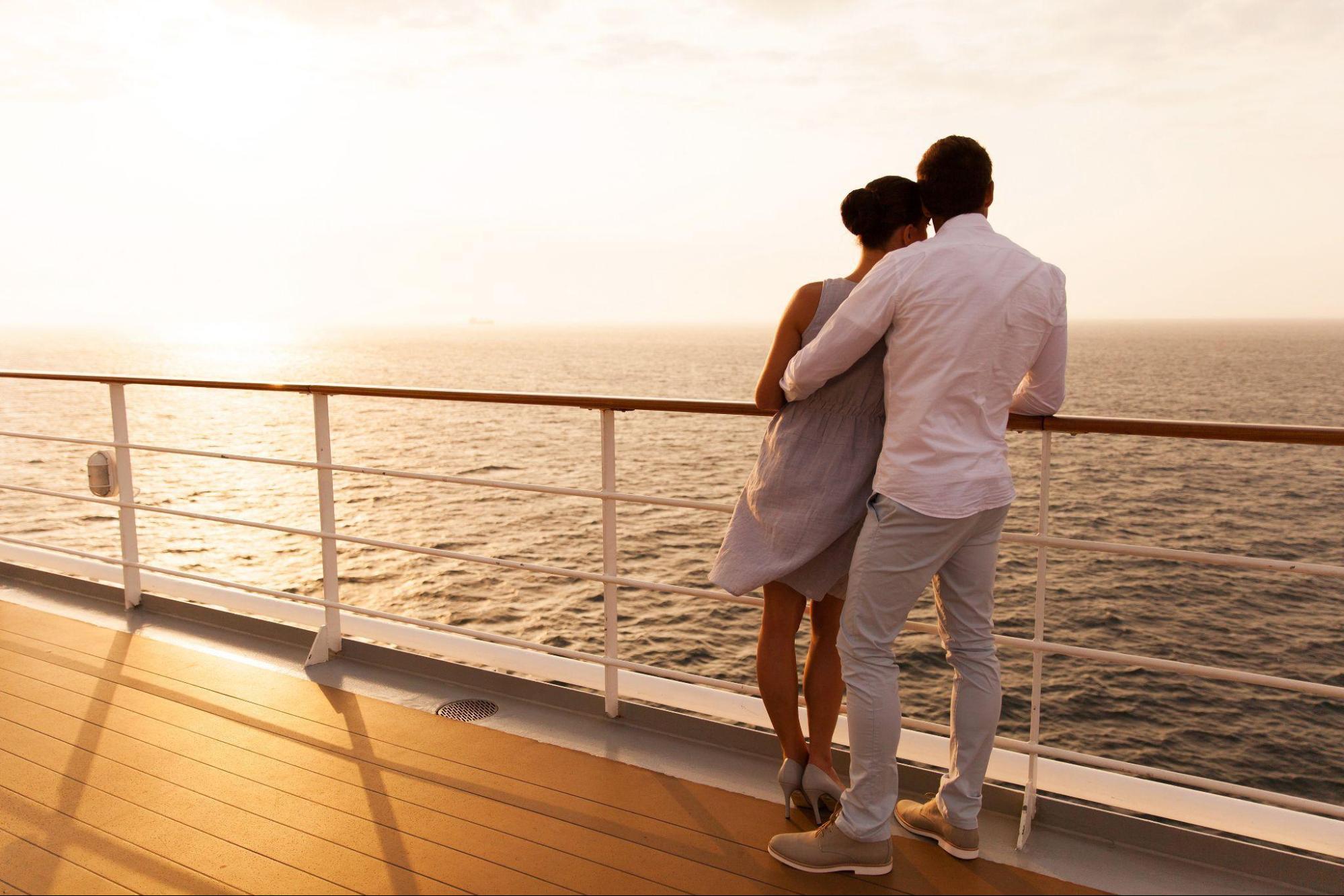 Ein Paar steht an der Reling eines Kreuzfahrtschiffes und blickt aufs Meer