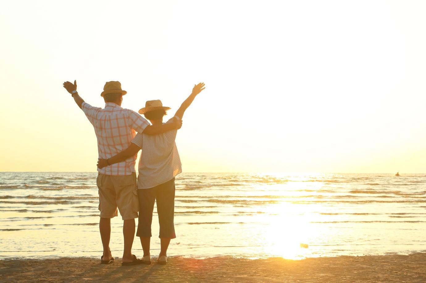Ein Paar steht mit erhobenen Armen am Rand des Strandes, während die Sonne untergeht